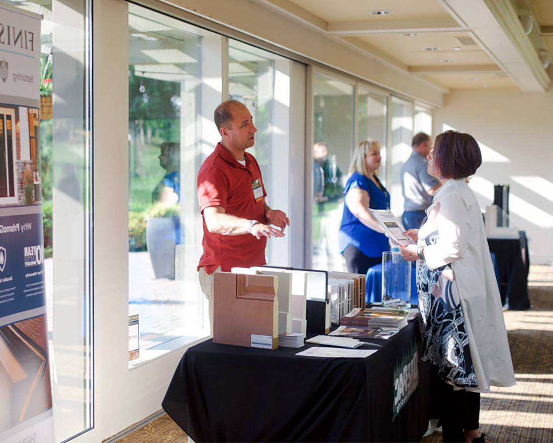 An OrePac representative shows samples of their different door products to an MBAKS member at an indoor event